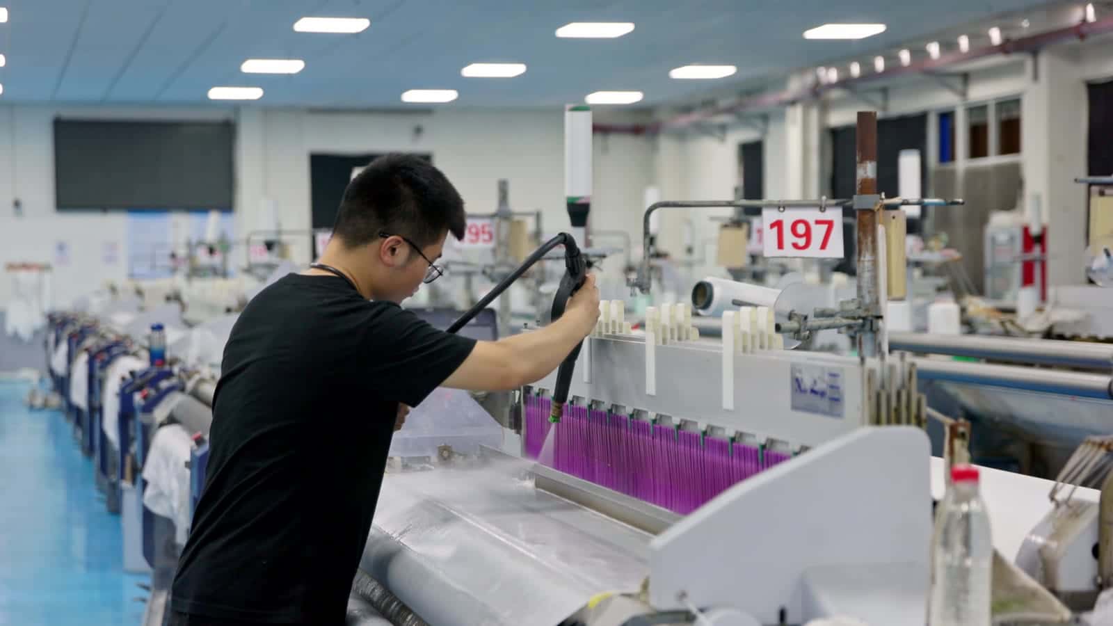 An operator working at a warping machine in a modern textile mill, rows of winding frames receding behind