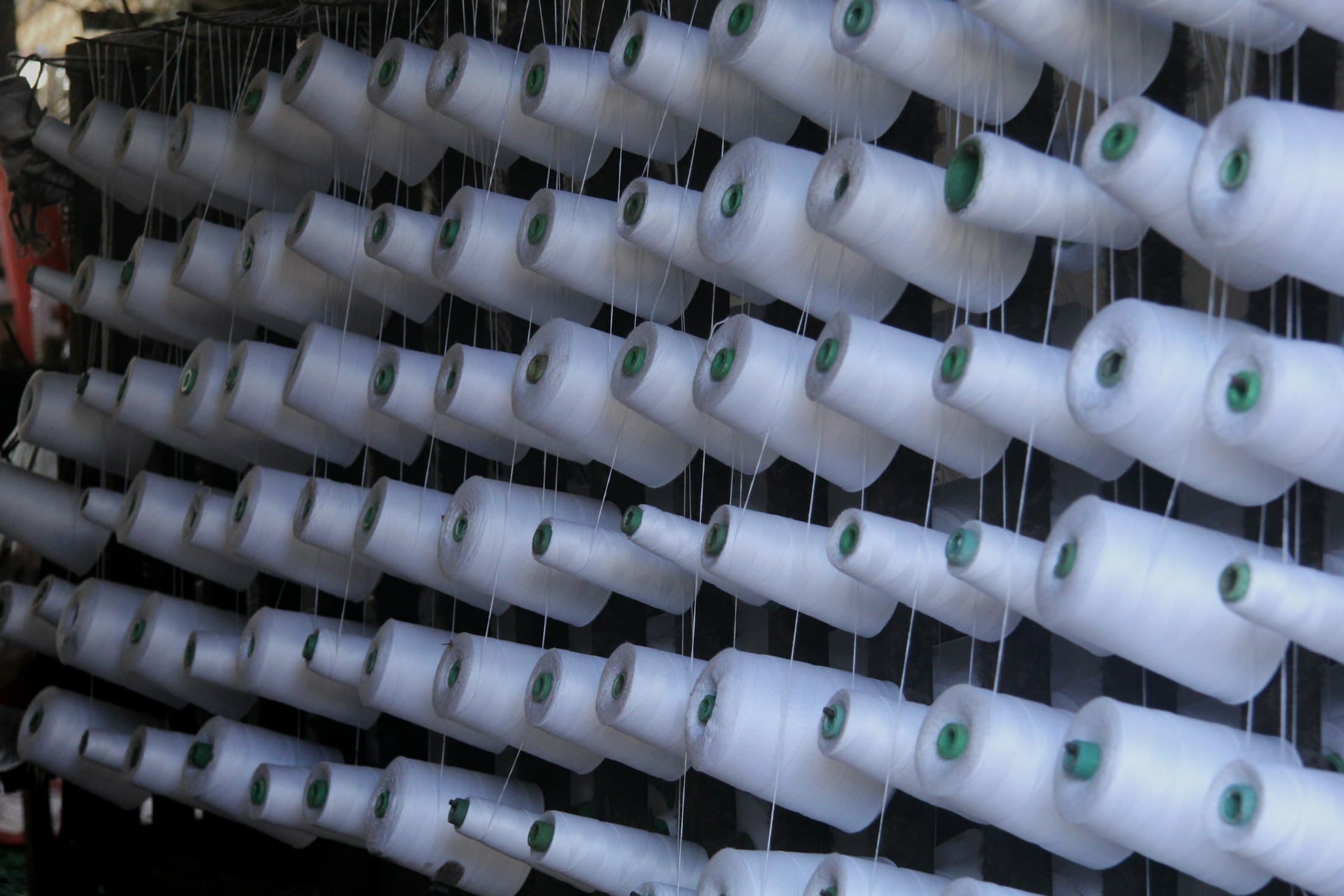 Dense rack of white yarn cones with threads drawn off under tension