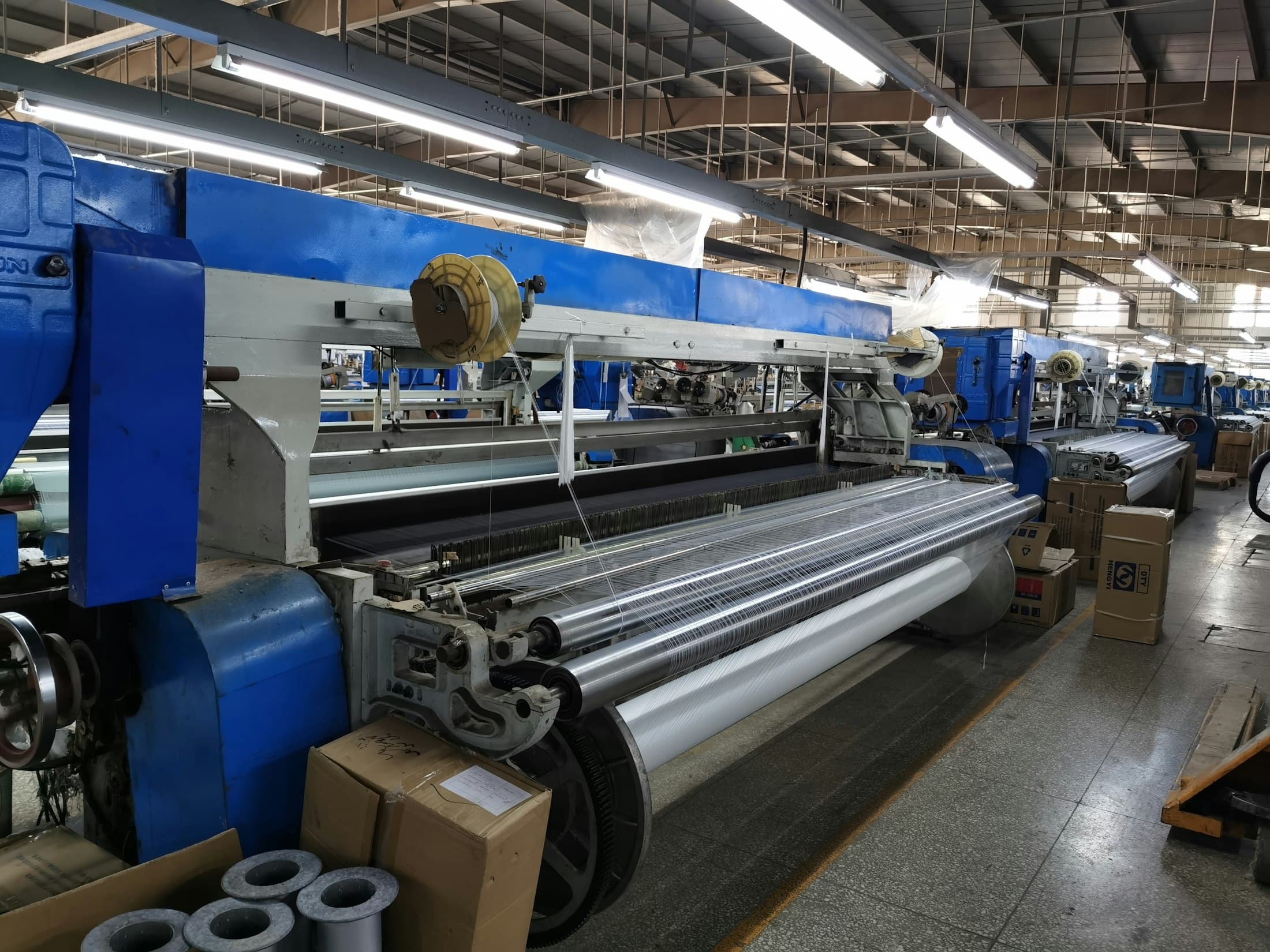 Wide-width shuttleless loom with the warp sheet running through the reed and cloth taking up on the roll