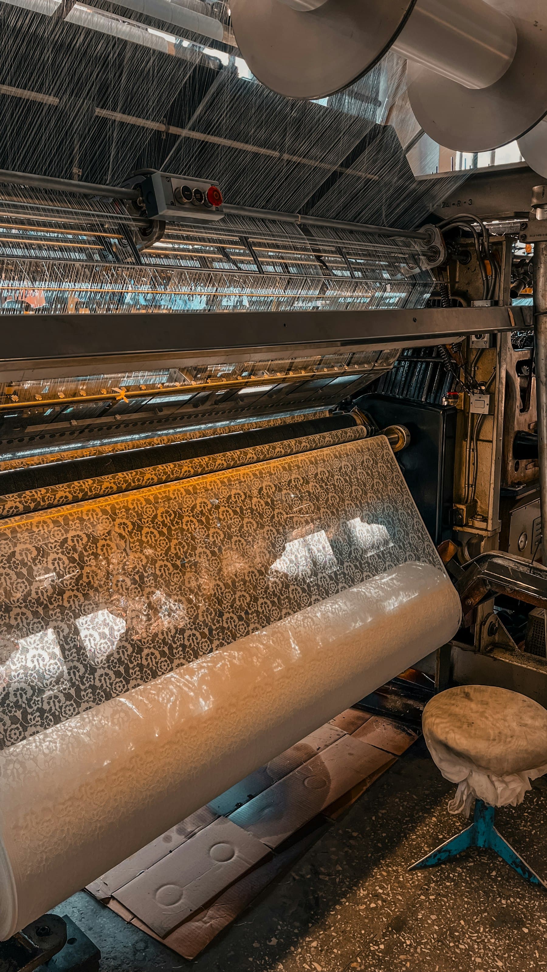 Working loom weaving patterned cloth, dense warp sheet overhead and finished fabric on the take-up roll