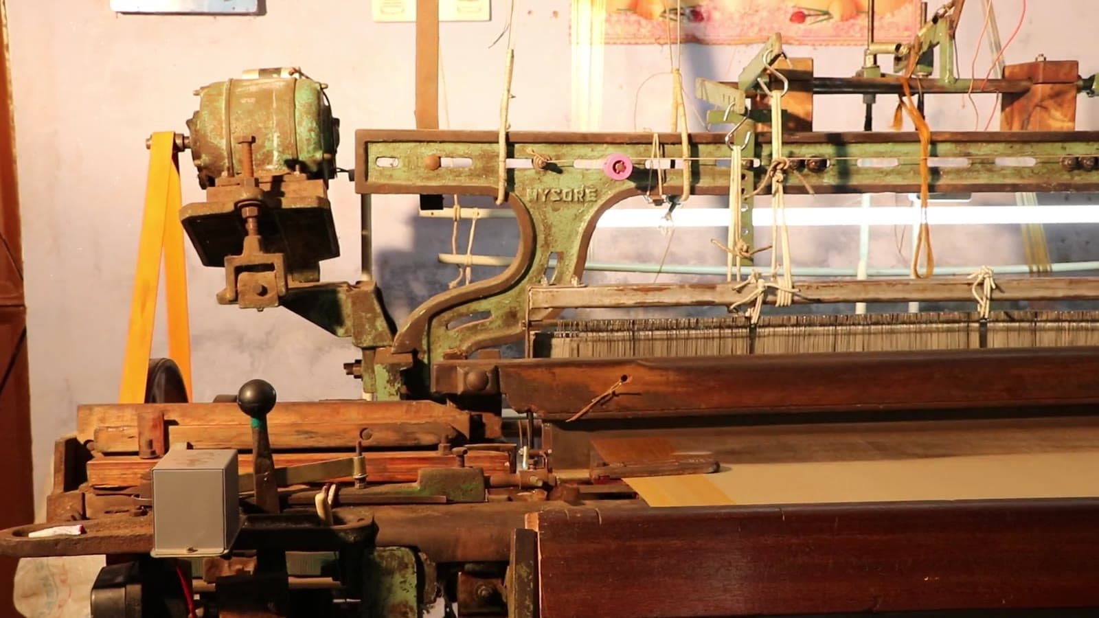 A powerloom running in a weaving shed, warp threads drawn through the heddles and cloth taking up on the roll